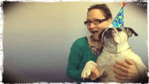 Emily Moran Barwick of Bite Size Vegan is shown with her beloved bulldog, Ooby, in her arms. Ooby has a small party hat upon her head.