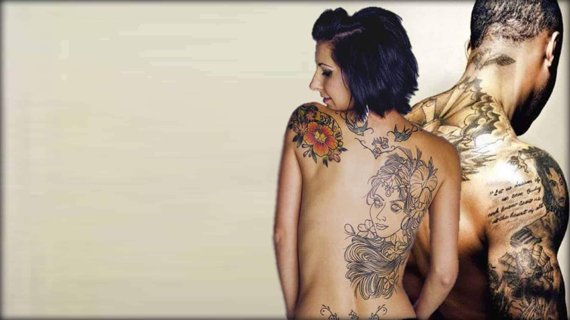 Two individuals are shown with their backs turned towards the camera. Both are topless. Both are displaying beautifully tattooed artwork on their backs and arms.