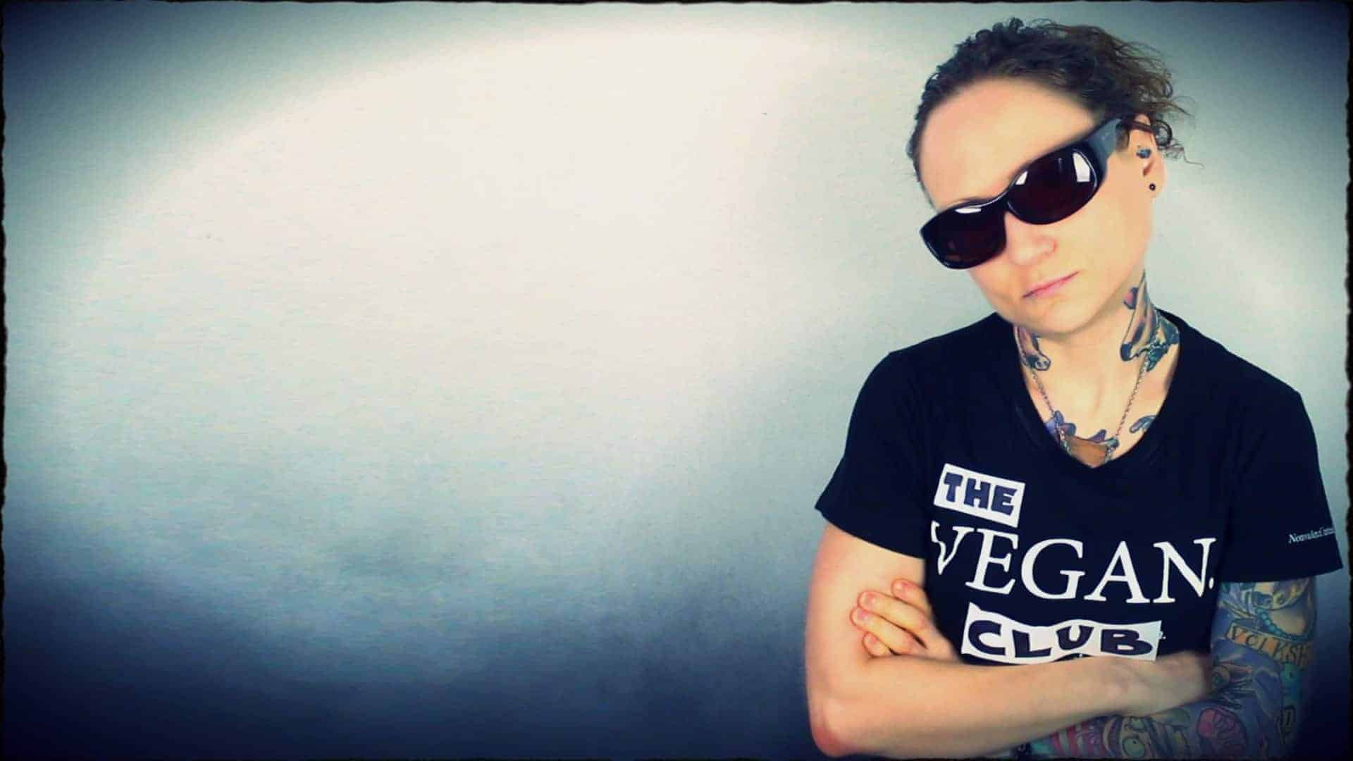 Emily Moran Barwick of Bite Size Vegan is shown in a dark tee-shirt and shades. Her tee-shirt says “The vegan club”. Emily’s head is tilted to one side and a look of intimidation is upon her face.