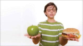 A person is shown holding an apple in one hand and a hamburger in the other. They appear to be weighing the decision of which to eat.