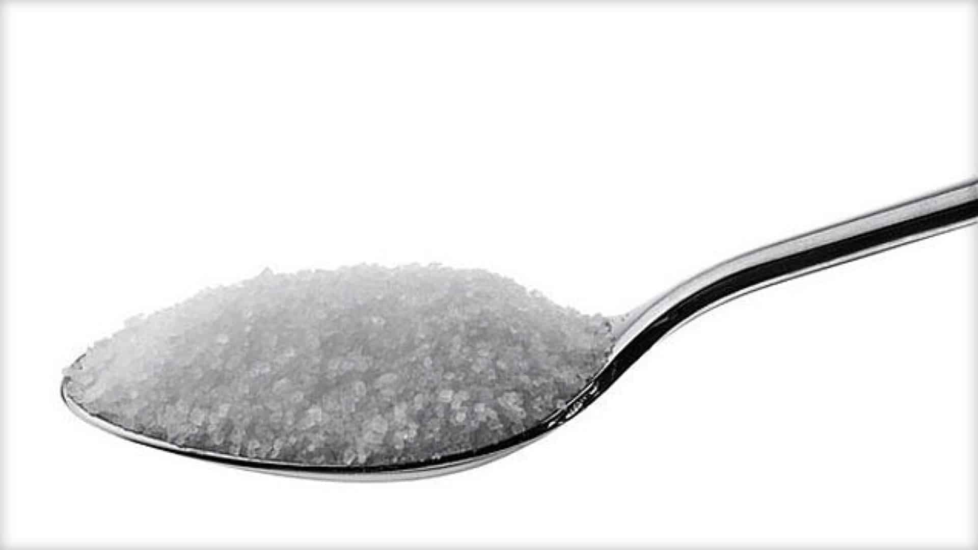 A spoon is shown in close-up, loaded with white sugar granuals.