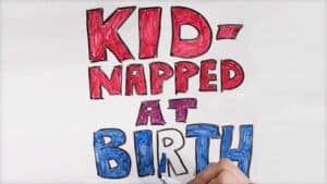 The words “Kid-napped at birth” are shown written on a whiteboard in colorful letters.