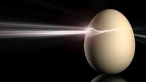 Against a dark background a white egg is shown balancing upon its end. The side of the egg has a small, open crack in it, near the top. Out of this crack a beam of bright light is seen to be streaming across and out of frame to the left.