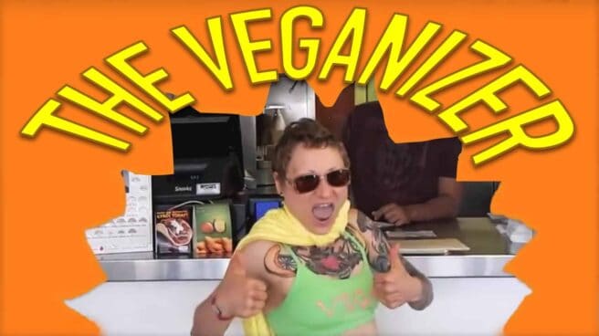 Emily Moran Barwick of Bite Size Vegan is shown dressed as the Veganizer superhero. The image makes it appear like she has punched her way through a wall. Across the top in large letters are the words “The Veganizer”
