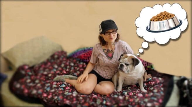 Emily Moran Barwick of Bite Size Vegan is shown relaxing with her beloved bulldog, Ooby, by her side. A thought bubble can be seen coming up from Ooby. Within it is an image of a dog bowl full of food.