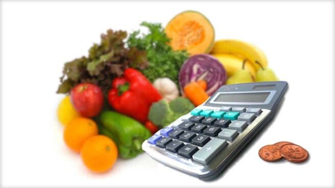 The image is made up of three elements. At the back is a glorious and colorful selection of fruit and vegetables. In front and to the side is a desk calculator. To the side of this are three coins.
