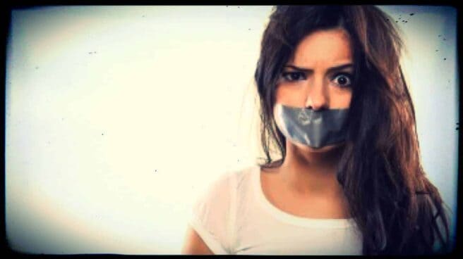 A person is shown from the shoulders up. They have grey tape across their mouth, silencing them. One eyebrow lifted in astonishment.