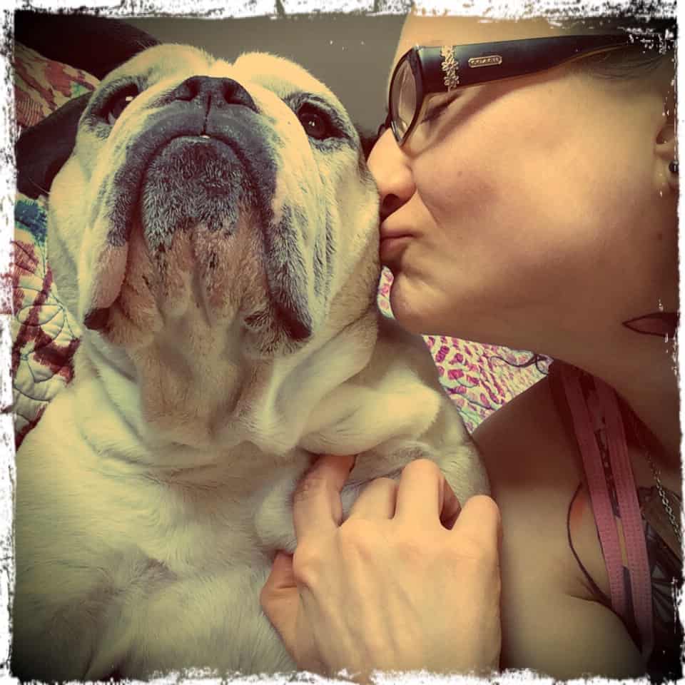 Emily Moran Barwick, founder of Bite Size Vegan, lovingly kissing the side of Ooby the bulldog's head.