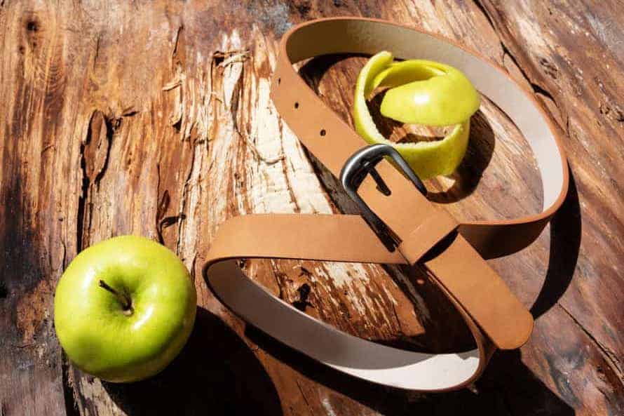 An apple next to a belt made from apple leather, a vegan leather alternative.