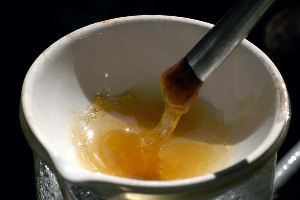 A brush being dipped into melted animal glue in a ceramic bowl.